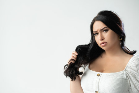 Dry hair. Displeased fatty woman. Haircare problem. Beauty salon. Advertising background. Gloomy brunette plus size lady holding locks isolated white copy space.の写真素材