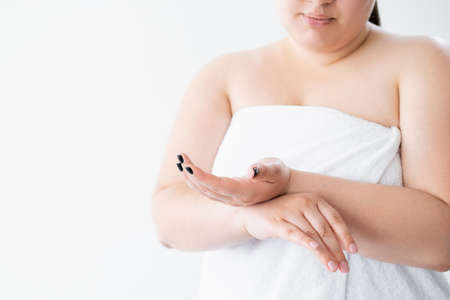 Body treatment. Plus size woman. Sensitive skin. Beauty procedure. Morning routine. Unrecognizable curvy lady covering towel touching hands after applying cream isolated white copy space.の写真素材