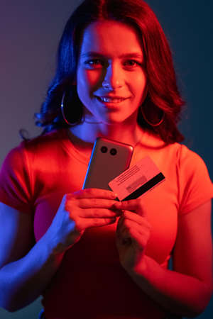 Secure payment. Cyber banking. Internet shopping. Cheerful smiling woman in neon bright red blue...