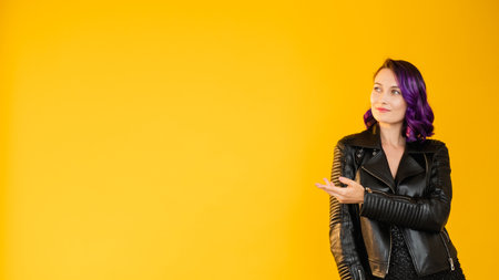 Black friday. Stylish woman. Presenting gesture. Holiday sale. Beautiful lady purple curly hair leather jacket pointing copy space isolated yellow. Advertising background.の写真素材