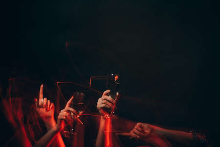 Night club party. Festive drink. Holiday joy. Unrecognizable man and woman holding glass of champagne hands dancing isolated black long exposure defocused red light copy space.の写真素材