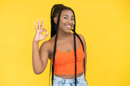 Okay gesture. Agreement sign. Good idea. Satisfied happy African woman showing ok approval hand symbol isolated on orange background.の写真素材
