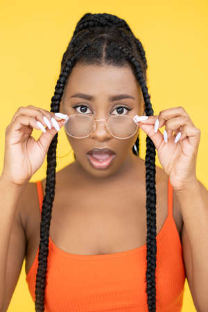 Shocked woman. Amazed expression. Unbelievable news. Surprised wow African lady face emotion in glasses with open mouth isolated on orange background.の写真素材