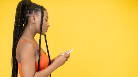 Phone messaging. Gadget banner. Online shopping. Side view of African woman internet browsing on cell isolated on orange empty space flyer.の写真素材