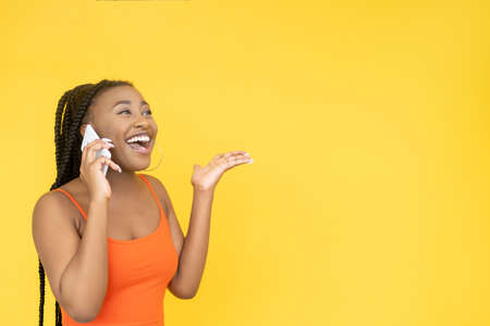 Winner call. Victory surprise. Mobile communication. Overjoyed excited African woman talking on phone isolated on orange empty space background.の写真素材
