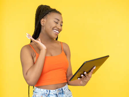 Video call. Online communication. Digital technology. Happy smiling Afro woman using PC tablet internet isolated on orange background.の写真素材