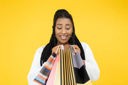 Shopping bonus. Black Friday. Giveaway offer. Pleased happy African woman with purchase market bags isolated on orange background.の写真素材