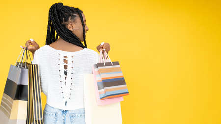 Sale shopping. Discount banner. Black Friday. Back view of Afro woman with purchase bags isolated on orange empty space background.の写真素材