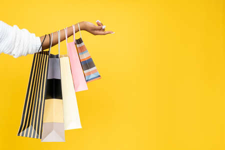 Sale offer. Black Friday. Shopping discount. Closeup of Afro woman hand holding purchase bags isolated on orange empty space background.の写真素材