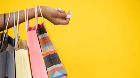 Shopping banner. Black Friday. Sale flyer. Closeup of African woman hand with shopper paper bags isolated on yellow copy space background.の写真素材