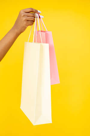 Shopping purchase. Black Friday. Sale discount. Closeup of African woman hand holding mall shopper bags isolated on orange background.の写真素材