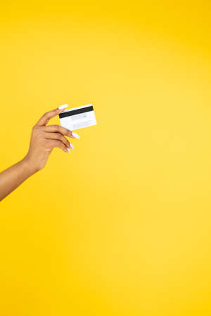 Banking operation. Cashback bonus. Loyalty program. Closeup of African woman hand holding credit card isolated on orange copy space background.の写真素材