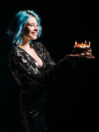 Birthday party. Happy woman. Holiday organization. Enjoying celebration. Inspired joyful lady blue hair holding festive cake candle lights isolated black.の写真素材