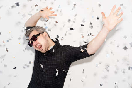 Party fun. Carefree celebration. Holiday entertainment. Festive occasion. Overjoyed happy man in sunglasses dancing enjoying weekend in confetti fall isolated on white background.の写真素材