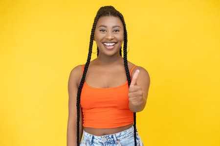 Approval gesture. Agree sign. Excellent idea. Joyful smiling African woman showing thumb up success symbol isolated on orange background.の写真素材