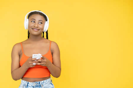 Mobile leisure. Millennial lifestyle. Modern technology. Happy African woman in earphones using...