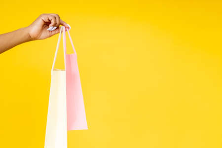 Purchase delivery. Online shopping. Retail promotion. Closeup of black woman hand holding bags isolated on orange empty space background.の写真素材