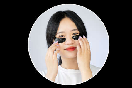 Asian beauty care. Rejuvenation cosmetic. Anti-aged treatment. Pretty smiling woman with black under eye pads isolated white dark circle frame.の写真素材