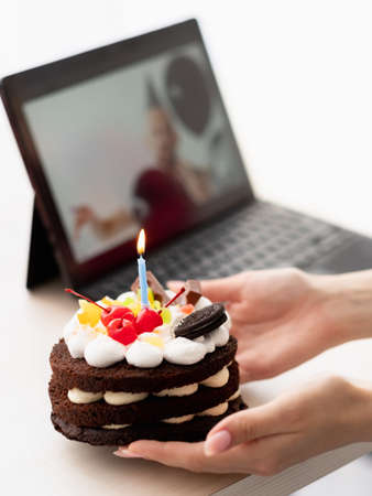 Virtual birthday. Festive cake. Online greeting. Unrecognizable woman holding holiday biscuits defocused laptop party man isolated white.の写真素材