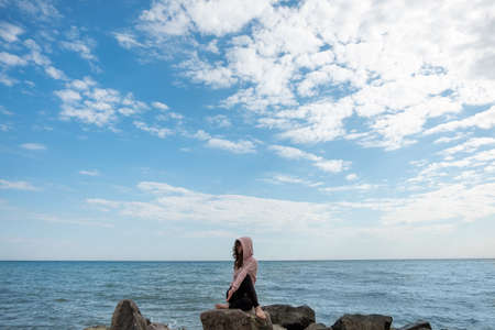 Yoga practice. Relaxed woman. Static pose. Peaceful lady sitting Gomukasana on rock stone azure water blue sky view.の写真素材