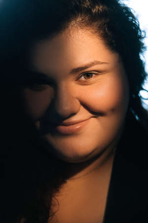 Overweight woman face. Facial care. Body positive. Beauty portrait of smiling obese lady with natural makeup flawless radiant smooth skin in warm light.の写真素材