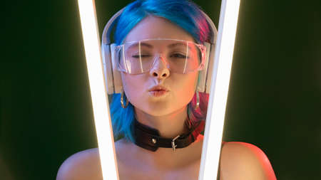 Blow kiss. Futuristic girl. DJ style. Pretty flirty winking woman in headphones pouts lips in LED...