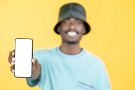 Mobile app. Hipster man. Advertising information. Happy defocused guy in stylish look holding smartphone blank white screen isolated yellow.の写真素材