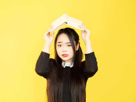 Worried student. School stress. Homework overload. Highschool education. Nervous scared teenager girl hiding under book on yellow background.の写真素材