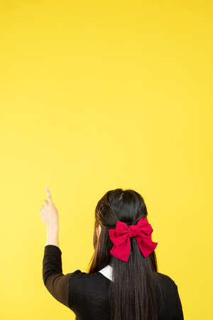Pointing girl. Product promotion. Advertising mockup. Unrecognizable woman presenting with index finger announcement on yellow copy space background.の写真素材