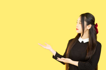 Demonstrating woman. Presentation advertising. Special offer. Recommending girl pointing at invisible product on yellow copy space background.の写真素材