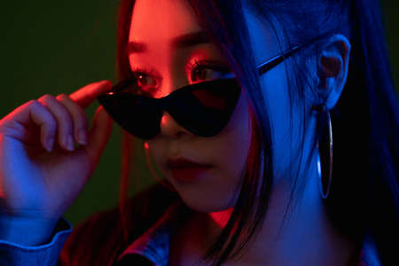 Neon woman face. Night portrait. Vaporwave style. Attractive cyberpunk model in stylish sunglasses in colorful red blue glowing light.の写真素材