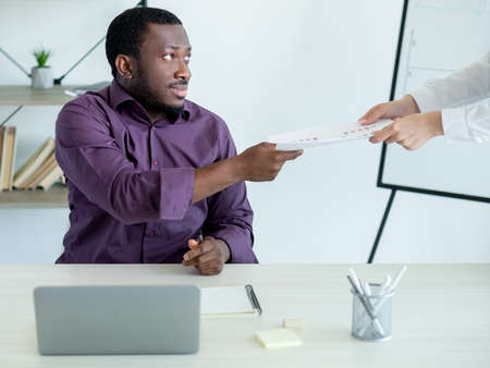 Office work. Colleagues cooperation. Do task. Male worker taking documents from woman sitting workplace in light room interior.の写真素材