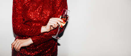 Party toast. Womans day. Festive celebration. Advertising background. Unrecognizable elegant lady in red paillette dress holding champagne glass isolated white copy space wide ledge.の写真素材