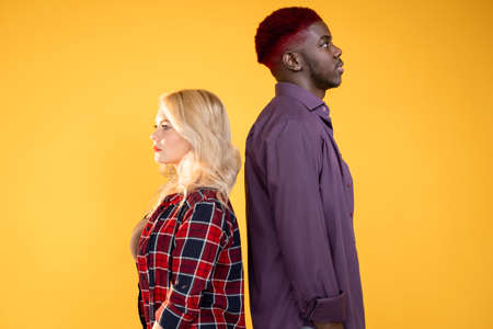 People diversity. Multiracial society. Human race. Different ethnicity. Side view of serious multiethnic couple African man Caucasian woman isolated on bright orange background.の写真素材