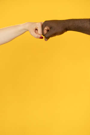 Multiracial respect. Stop racism. Racial diversity. International cooperation. Mixed race African man white woman bump fist in partnership unity isolated on orange copy space.の写真素材