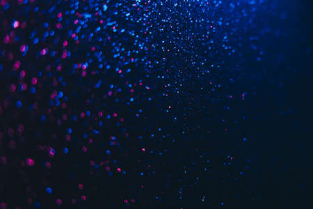 Bokeh sparks. Neon glitter background. Festive glow reflection. Defocused blue pink color light shimmering circles pattern on dark black abstract overlay.の写真素材