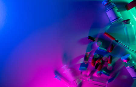 Pharmaceutical background. Coronavirus drug. Lab research. Neon light vaccine jab dose bottle syringe pills test tube arrangement on bright pink blue colorful empty space.の写真素材