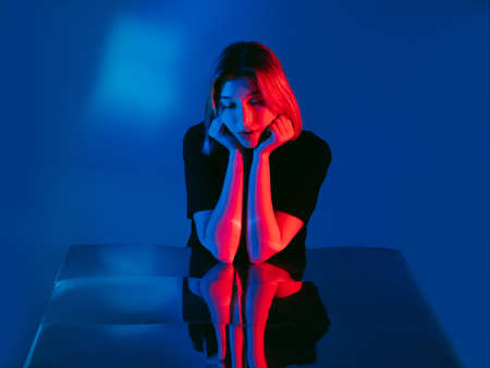 Sad woman. Neon light portrait. Loneliness melancholy. Upset depressed pensive girl in pink blue color gradient glow isolated on dark copy space background.の写真素材