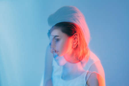 Double exposure portrait. Sensitive woman. Tenderness fragility. Red neon color light defocused silhouette of pensive female face isolated on blue out of focus.の写真素材