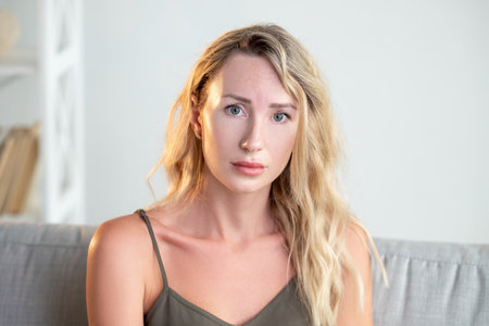 Upset situation. Regretful woman. Disappointed look. Sad pretty lady feeling sorrow sitting sofa in light room interior.の写真素材