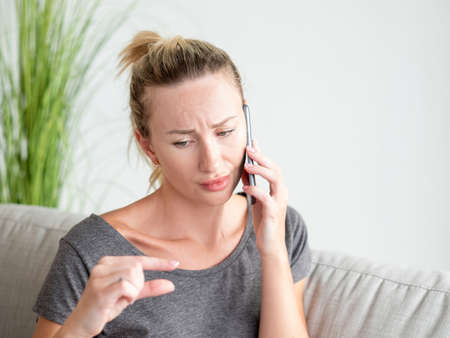 Measurement gesture. Sad woman. Mobile communication. Pretty unhappy lady showing fingers sign of small size talking smartphone light room interior.の写真素材