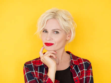 Puzzled woman. Uncertain situation. Think over problem. Doubtful middle-aged lady considering idea holding hand on chin isolated yellow.の写真素材