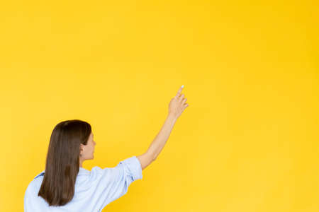 Pointing gesture. Searching woman. Advertising background. Unrecognizable lady holding hand on copy space isolated yellow.の写真素材