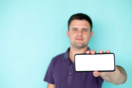 Mobile operator. Advertising man. Digital technology. Smiling defocused guy showing smartphone blank screen posing isolated blue copy space.の写真素材