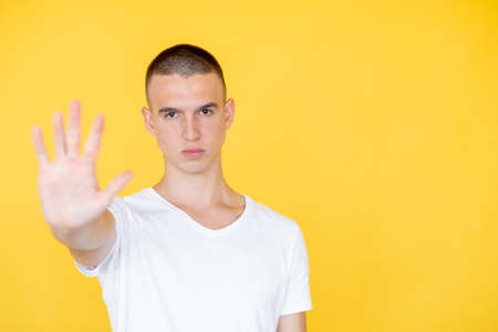 Stop gesture. Strict man. Closed way. Serious gloomy defocused guy in t-shirt holding forbidden hand...