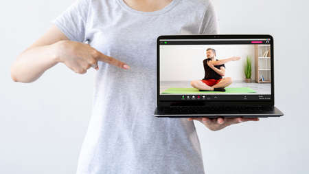Fitness online. Virtual gym. Home workout. Woman recommending sport video class pointing at laptop with man performing stretching exercise on screen isolated on light free space.の写真素材