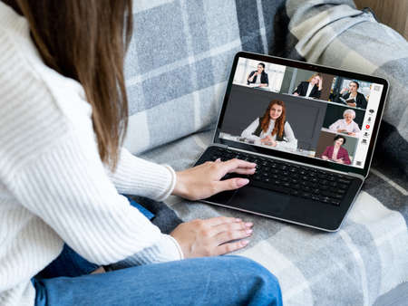 Home telework. Group video chat. Distance cooperation. Relaxed woman using laptop on couch working...