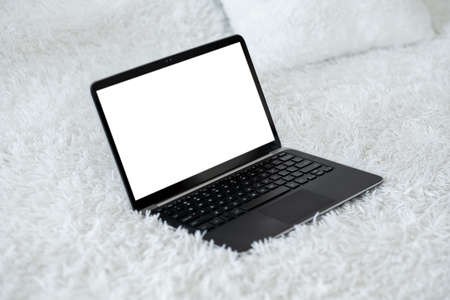 Digital life. Computer mockup. Online connection. Opened laptop with blank screen laying fluffy bed cover in light room interior.の写真素材