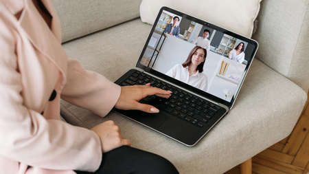 Video conference. Remote business. Telecommuting network. Female employee working online discussing strategy with diverse team on laptop screen on couch at home office.の写真素材