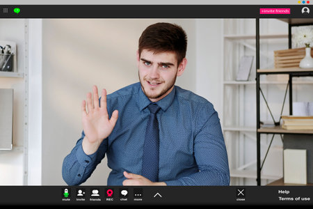 Online education. Greeting man. Screen mockup. Positive elegant guy sitting work desk showing hi gesture having webinar in light room interior.の写真素材